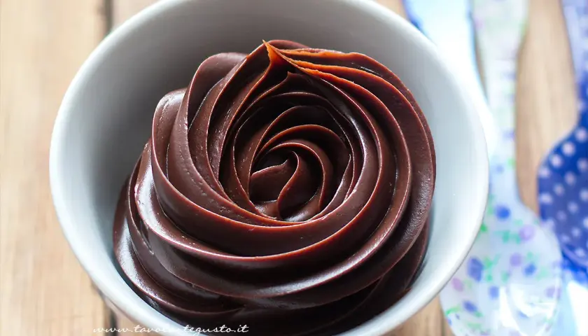 Una spirale di ganache cioccolato per copertura, lucida e invitante, in una ciotola bianca.