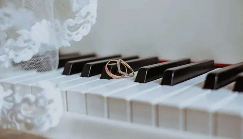 Dwa obrączki na klawiszach pianina, obok białej koronki.
