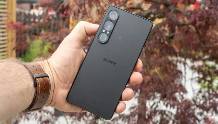 Czarny smartfon marki Sony z potrójnym aparatem, trzymany w dłoni na tle jesiennych liści.