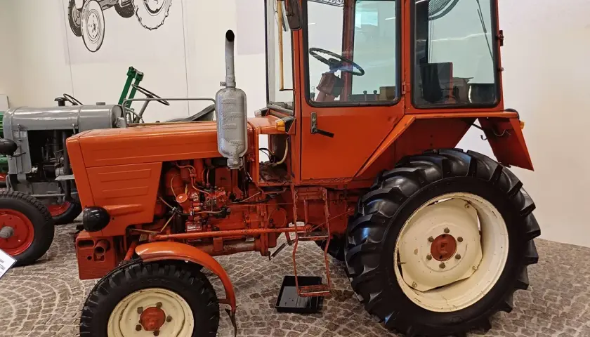 Pomarańczowy, odrestaurowany Władimirec T25 nowy, z kabiną i dużymi kołami, gotowy do pracy na polu.