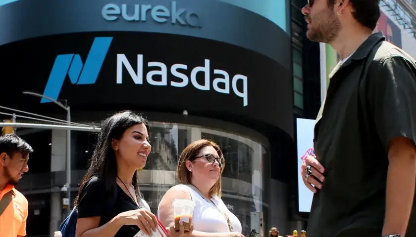 Ludzie przed budynkiem Nasdaq, gdzie handluje się akcjami. Słońce świeci, tworząc cień.