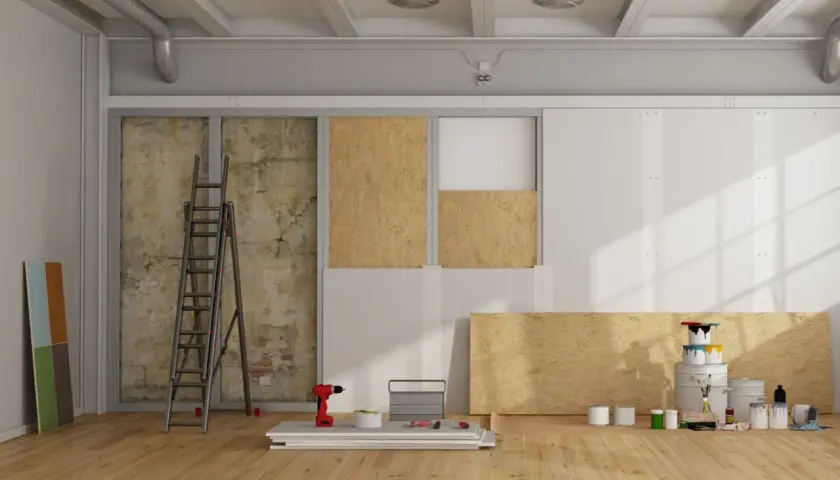 Chantier de rénovation avec panneaux de bois, échelle, outils et pots de peinture.