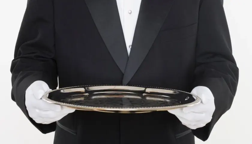 Ein Butler in schwarzem Frack mit weißer Weste und Handschuhen hält ein Silbertablett. Der Butler gehalt ist ein wichtiger Faktor für den Service.