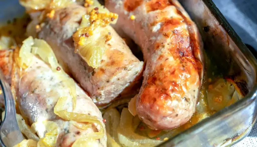Soczysta biała kiełbasa pieczona w cebuli i musztardzie, podana w szklanym naczyniu.
