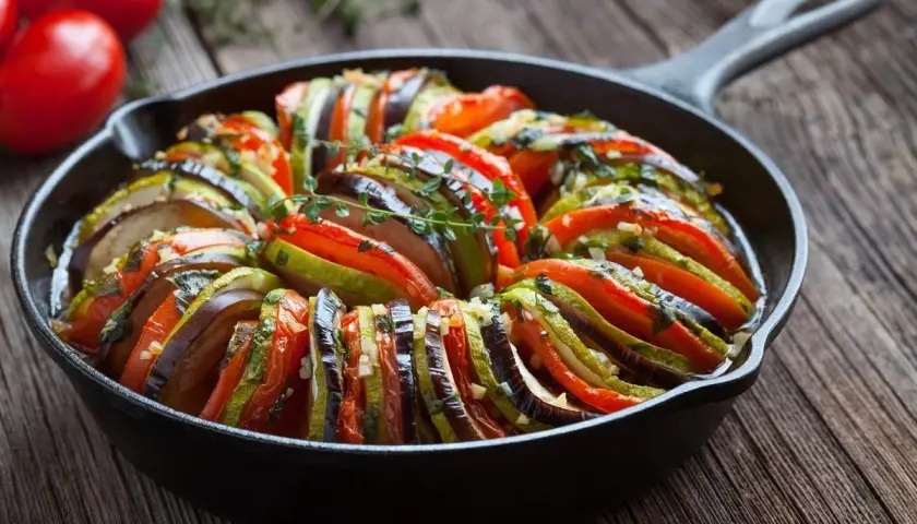 Ratatouille, jedno z popularnych dań francuskich, w naczyniu żeliwnym. Warzywa ułożone w wachlarz, ozdobione ziołami.
