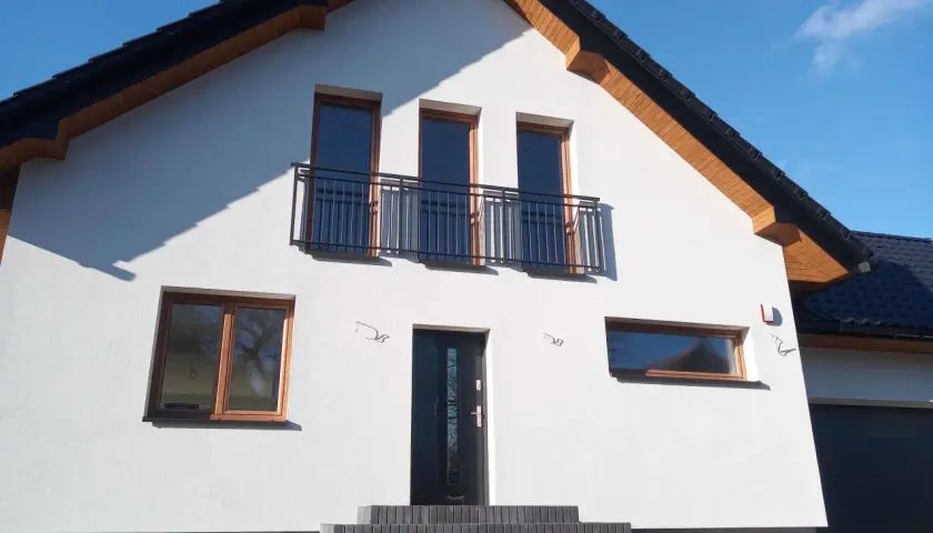 Nowy dom z białym tynkiem, antracytowym dachem i oknami w kolorze winchester.