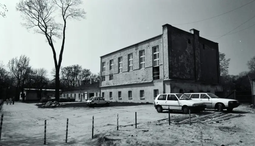 Zamek Ujazdowski w Warszawie, otoczony drzewami, z kilkoma samochodami na dziedzińcu.