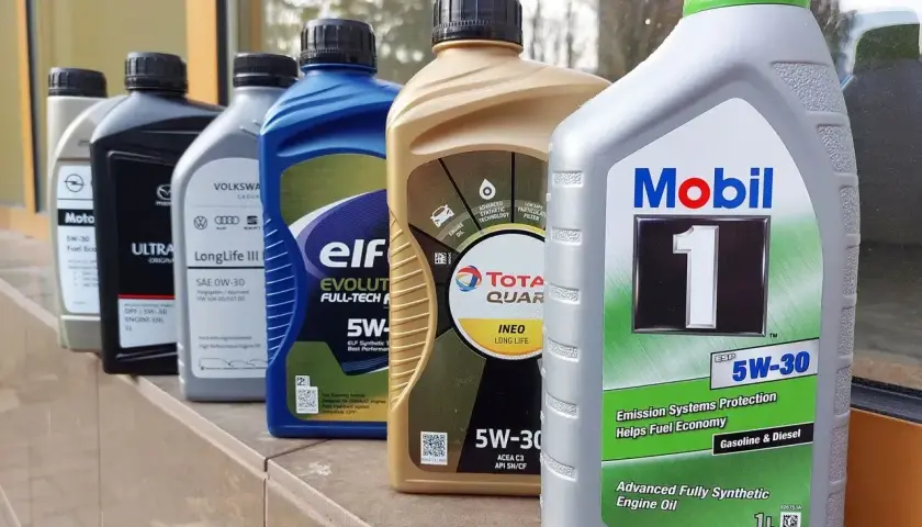 Różne oleje silnikowe, w tym 0w30 i 5w30, stoją w rzędzie. Widać marki takie jak Mobil 1, Elf, Total Quartz i Volkswagen.