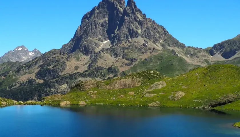 Lago azul intenso reflejando picos rocosos y verdes laderas en los Pirineos Francia.