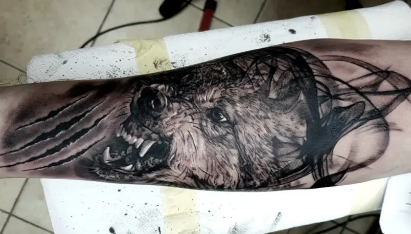 Tatuaż wilk z niebieskimi oczami, z kłami i pazurami, otoczony dymem i mgłą.