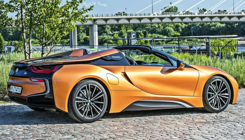 Pomarańczowy BMW i8 Roadster na bruku, pod mostem. Sprawdź aktualną bmw i8 cena.