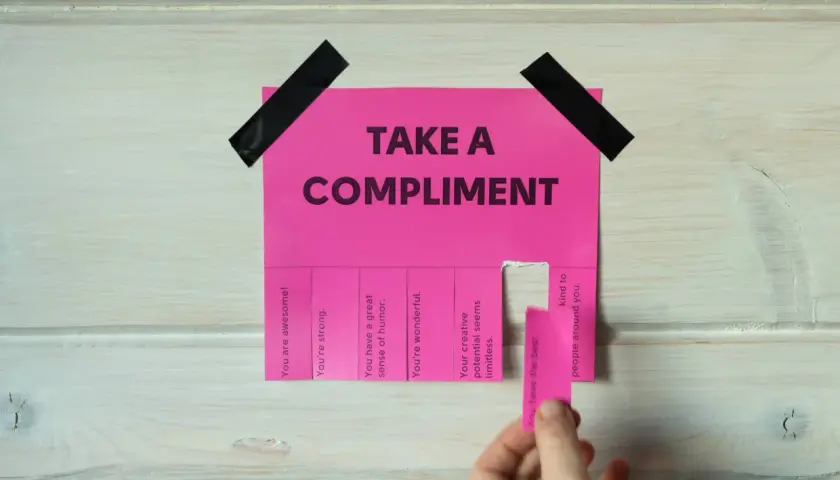 Różowa kartka z napisem "TAKE A COMPLIMENT" i odrywanymi kuponami z pochwałami. Daje to pomysł na inteligentne odpowiedzi na komplementy.