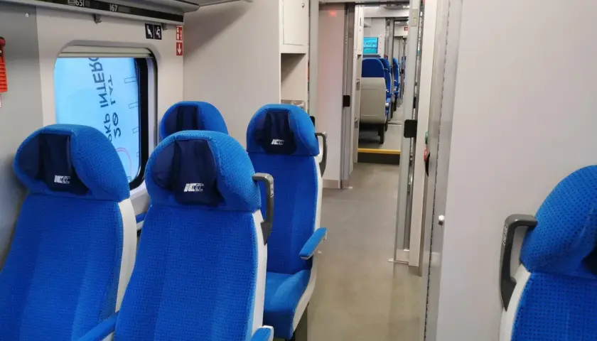 Wnętrze pociągu ed74 z niebieskimi siedzeniami i przejściem.