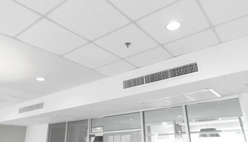 Soffitto modulare bianco con faretti, bocchette di ventilazione e un sistema di controsoffitto autoportante che nasconde gli impianti.