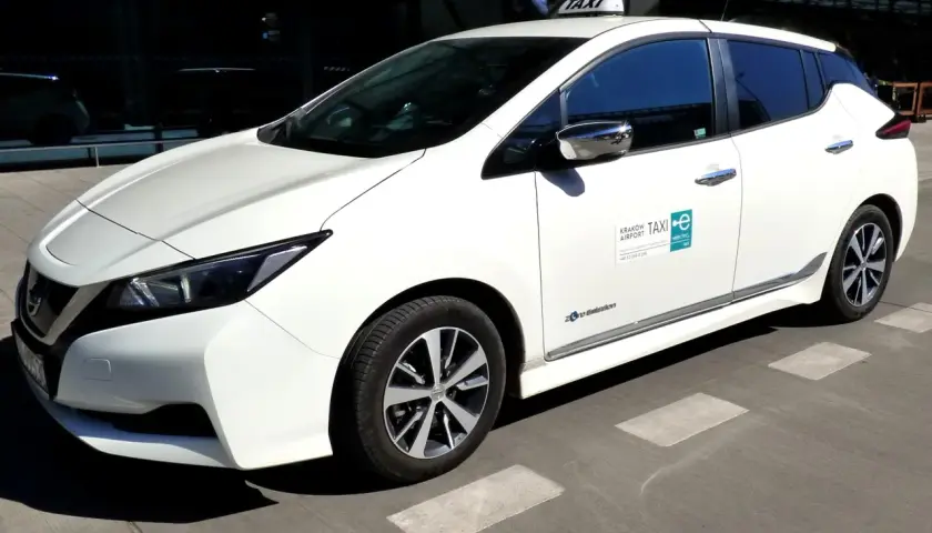 Białe taxi z lotniska Balice, elektryczne, gotowe do jazdy. Zastanawiasz się, ile kosztuje taxi z lotniska Balice do centrum Krakowa?