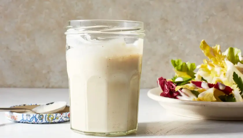 A jar of creamy miso dressing sits next to a fresh salad, ready to add a savory umami kick.