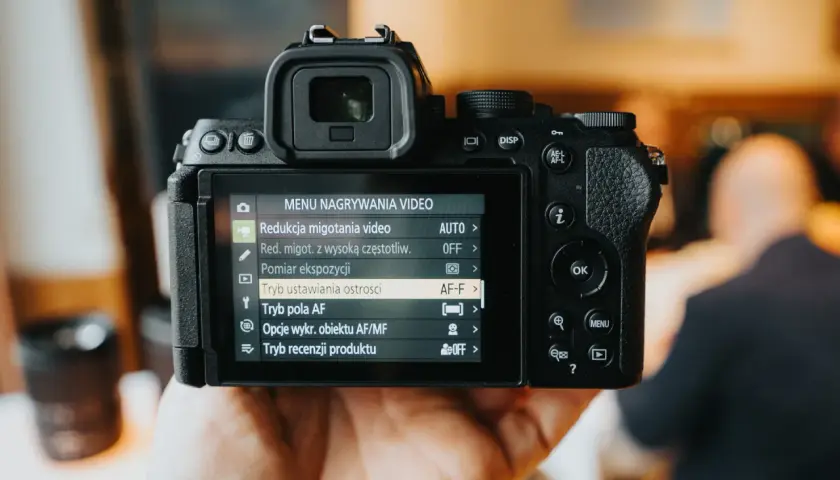 Dłoń trzyma aparat fotograficzny z włączonym menu nagrywania wideo.