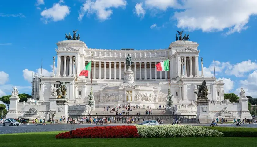 Il Vittoriano, uno dei monumenti famosi di Roma, con bandiere italiane e cielo azzurro.