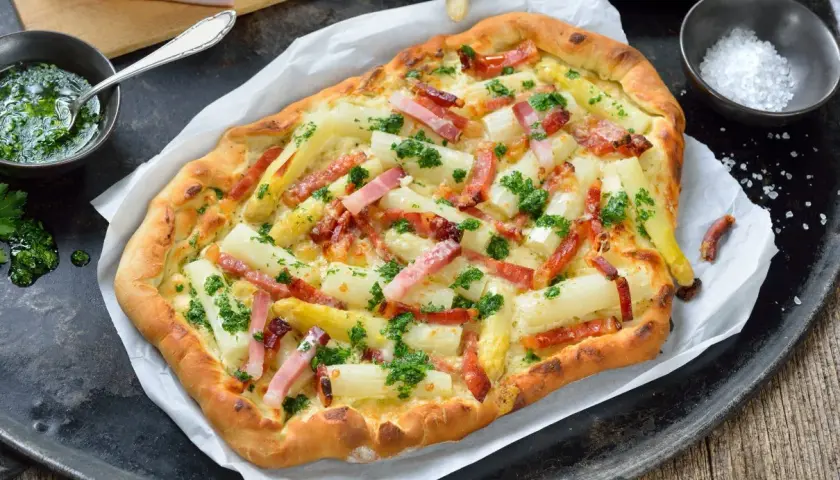 Pyszna pizza ze szparagami i boczkiem, posypana świeżą natką pietruszki. Idealna na wiosenny obiad.