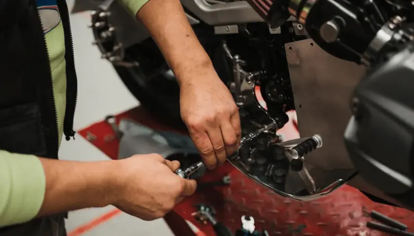 Mecánico realizando el cambio de aceite a una moto, usando herramientas para acceder al motor.