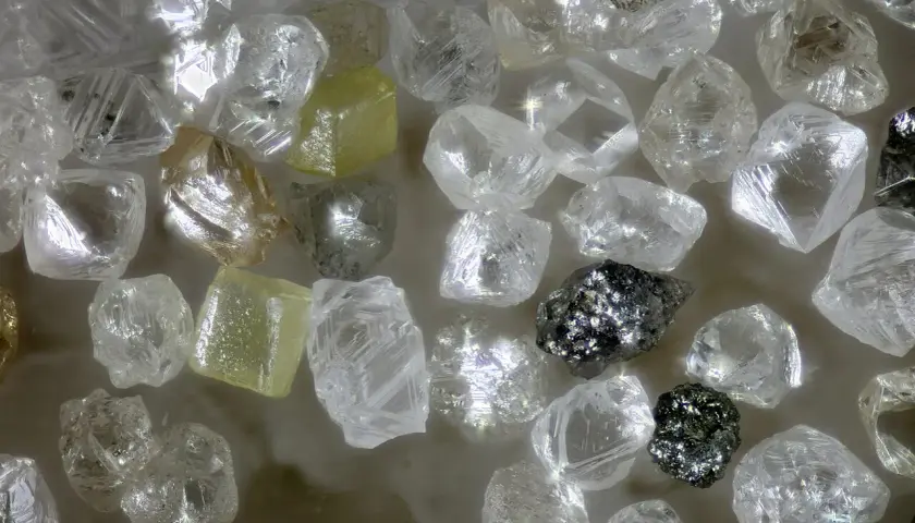 Unbearbeitete Diamanten, einige gelblich, andere klar, glänzen. Ihre Seltenheit und Härte erklären, warum sind Diamanten so wertvoll.
