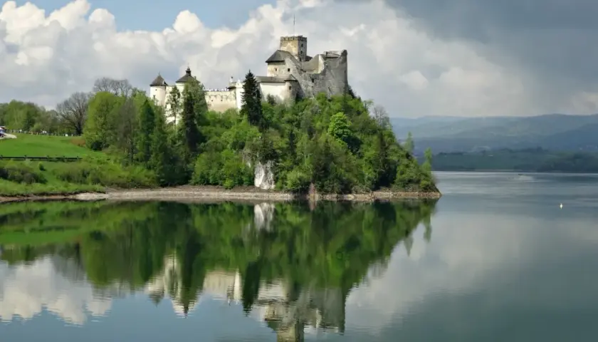 Zamek w Niedzicy dumnie wznosi się na wzgórzu nad jeziorem, odbijając się w spokojnej tafli wody.