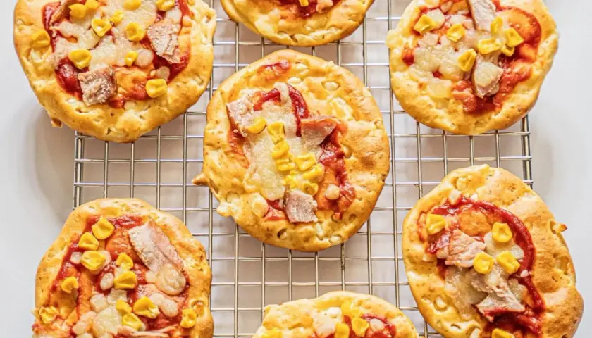 Mini pizze z serka wiejskiego, z kukurydzą i kawałkami mięsa, na metalowej kratce.