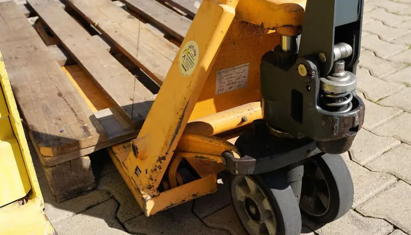 Ein Hubwagen hebt eine Holzpalette an. Dies ist ein gängiges Werkzeug im Lager, um Waren zu bewegen.