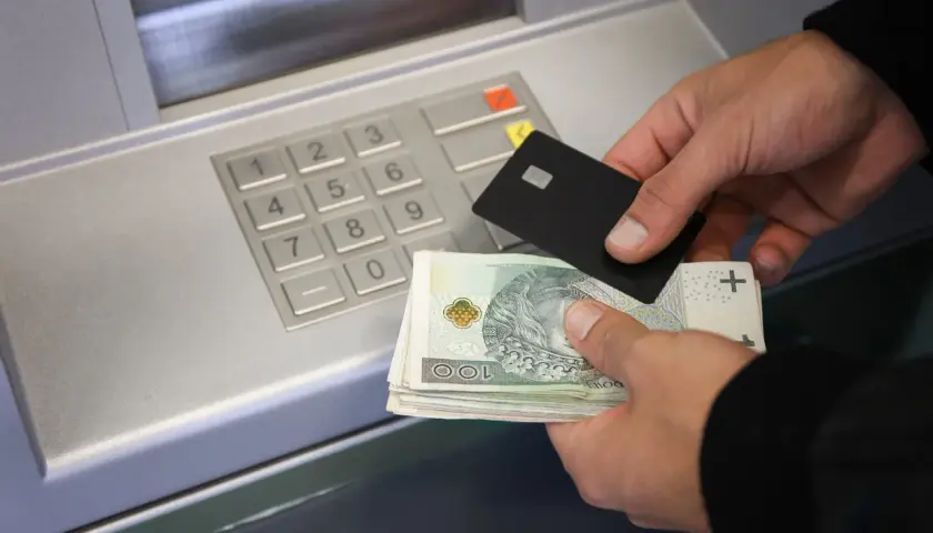 Ręce trzymające kartę i banknoty przy bankomacie, pokazujące, jak wpłacić pieniądze na konto.
