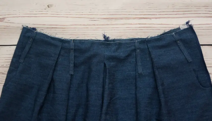 Close-up of a denim garment's waistband, showcasing various types of belt loops being prepared for sewing.
