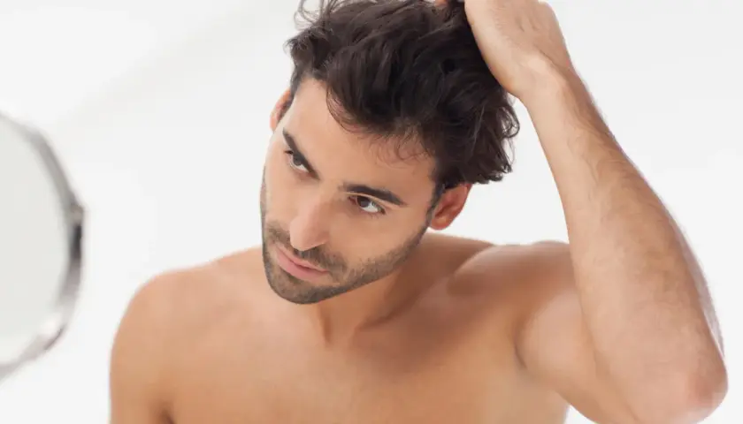 Hombre revisando su cabello en el espejo, parte de su rutina de cuidado del cabello hombre.