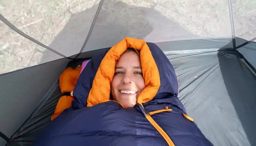 Smiling woman bundled in a navy and orange rei magma 15 weight sleeping bag inside a tent.