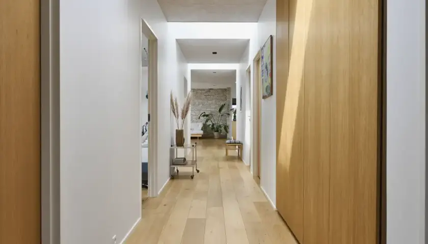 Un luminoso vano di disimpegno con pavimenti in legno chiaro, pareti bianche e armadi in legno.