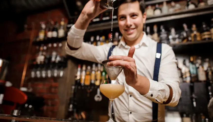 Uśmiechnięty barman przelewa drinka przez sitko. Czy barman może pić w pracy? Ten z pewnością tworzy pyszne koktajle!