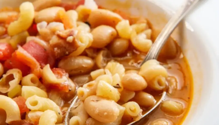 Un cucchiaio raccoglie un saporito piatto di pasta e fagioli, con maccheroni, fagioli bianchi e pomodoro in un brodo ricco.