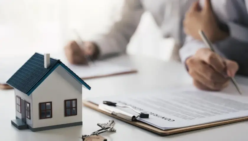 Maquette de maison, clés et contrat sur une table. Des mains signent des documents, symbolisant le **délai achat maison**.