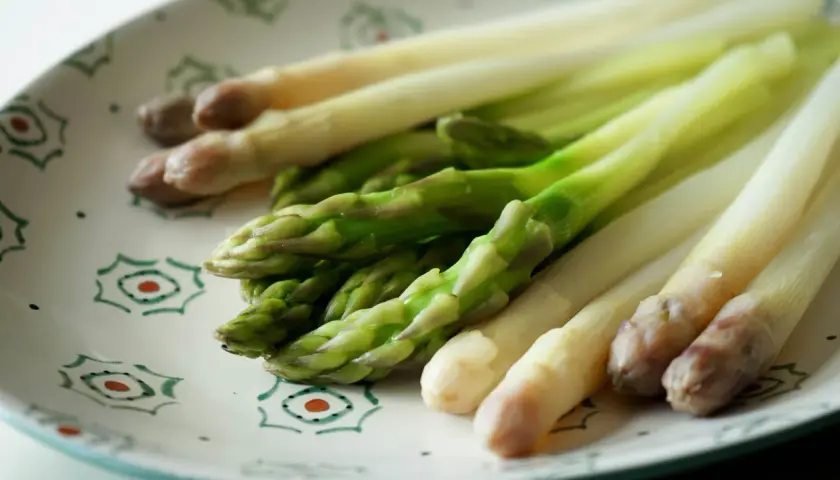 Asperges vertes et blanches sur une assiette décorée, prêtes pour la cuisson.