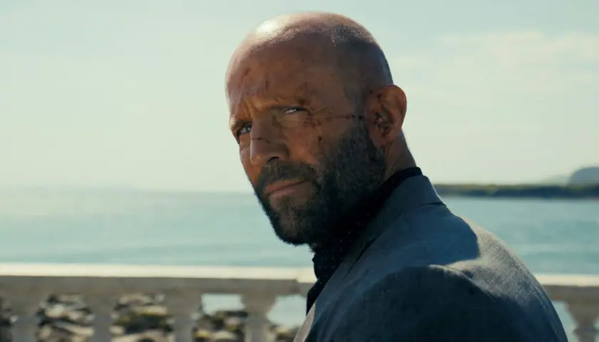 En skadad man med skägg och rakad skalle, klädd i kavaj, blickar ut över havet. En scen från biodlaren film.