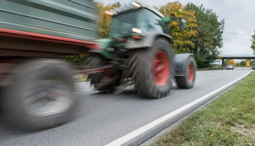 Ein Traktor mit Anhänger fährt auf einer Landstraße. Ab wann darf man Traktor fahren? Das ist eine wichtige Frage für junge Landwirte.