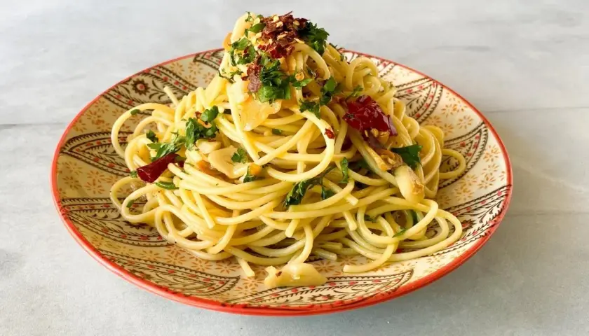 Un plato de spaghetti aglio e olio, con ajo laminado, perejil fresco y hojuelas de chile rojo, servido en un plato decorado.