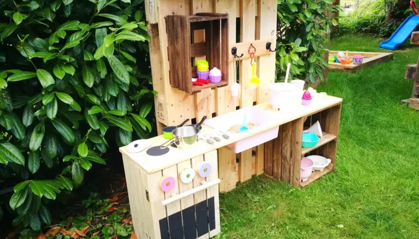 Kreative alte Weinkisten Deko Ideen: Kinderküche aus Paletten und Kisten im Garten, mit Spielzeuggeschirr und Sandkasten im Hintergrund.