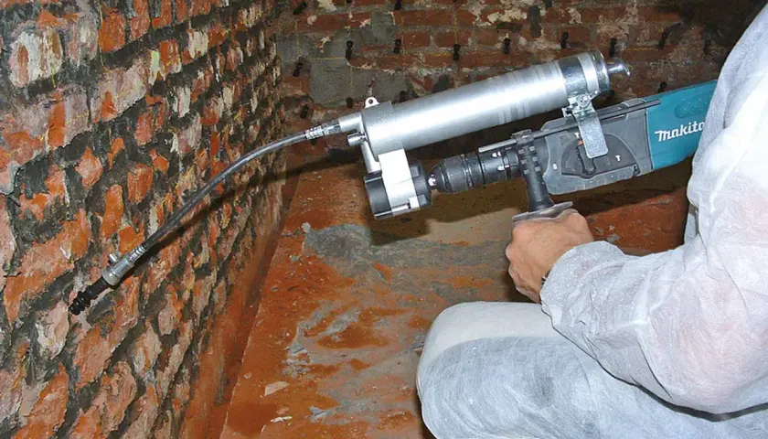 Person im Schutzanzug führt ein Injektionsverfahren selber machen durch, um eine feuchte Wand zu sanieren.