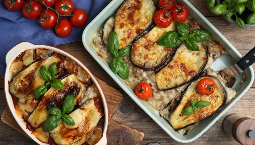 Deux plats d'aubergine à la parmesane au four, dorés et gratinés, garnis de tomates cerises et de basilic frais.