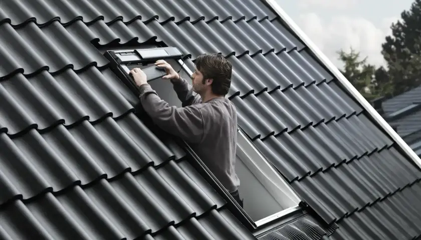 Uomo sul tetto che installa una finestra, la casa prende luce dal tetto.
