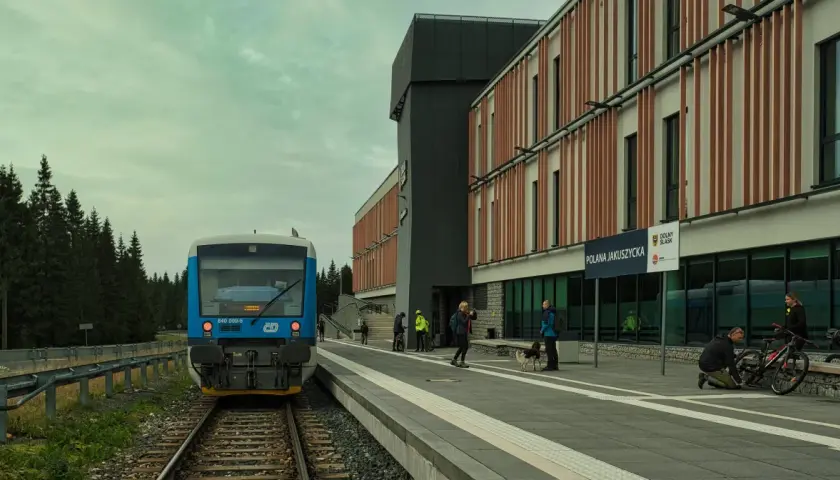 Niebieski pociąg na peronie Polany Jakuszyckiej, najwyżej położonej stacji kolejowej w Polsce. W tle nowoczesny budynek i las.