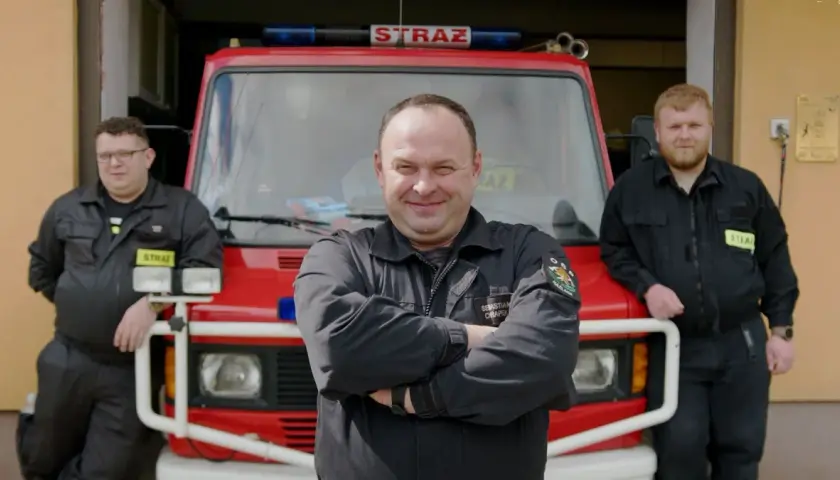 Trzech strażaków OSP pozuje przed wozem strażackim.
