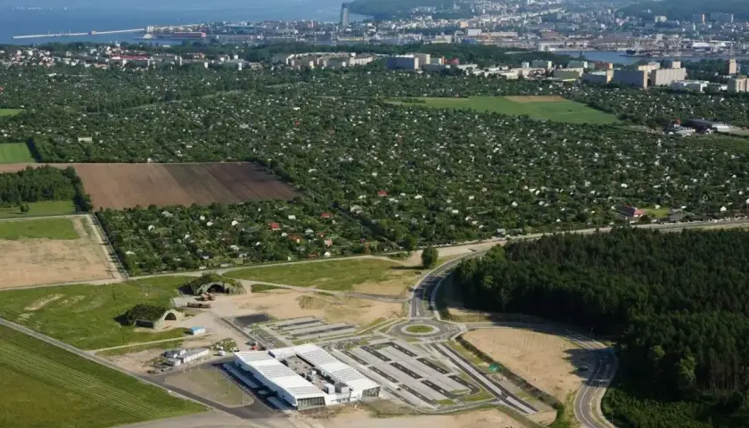 Widok na lotnisko Kosakowo z nowymi budynkami i drogami, w tle rozległe ogródki działkowe i panorama Gdyni.