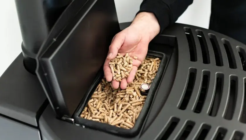 Dłoń wsypuje tani pellet z Czech do zasobnika nowoczesnego pieca.