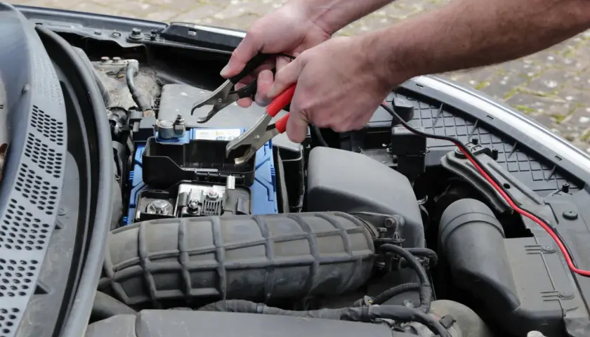 Ręce podłączają kable rozruchowe do akumulatora, bo diesel nie odpala za pierwszym razem.