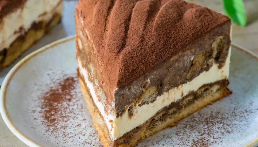Pyszny kawałek ciasta cappuccino na biszkopcie, posypany kakao. Idealny przepis na deser.